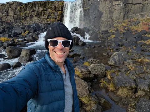 Nathan in a beanie and sunglasses in front of Öxarárfoss waterfall